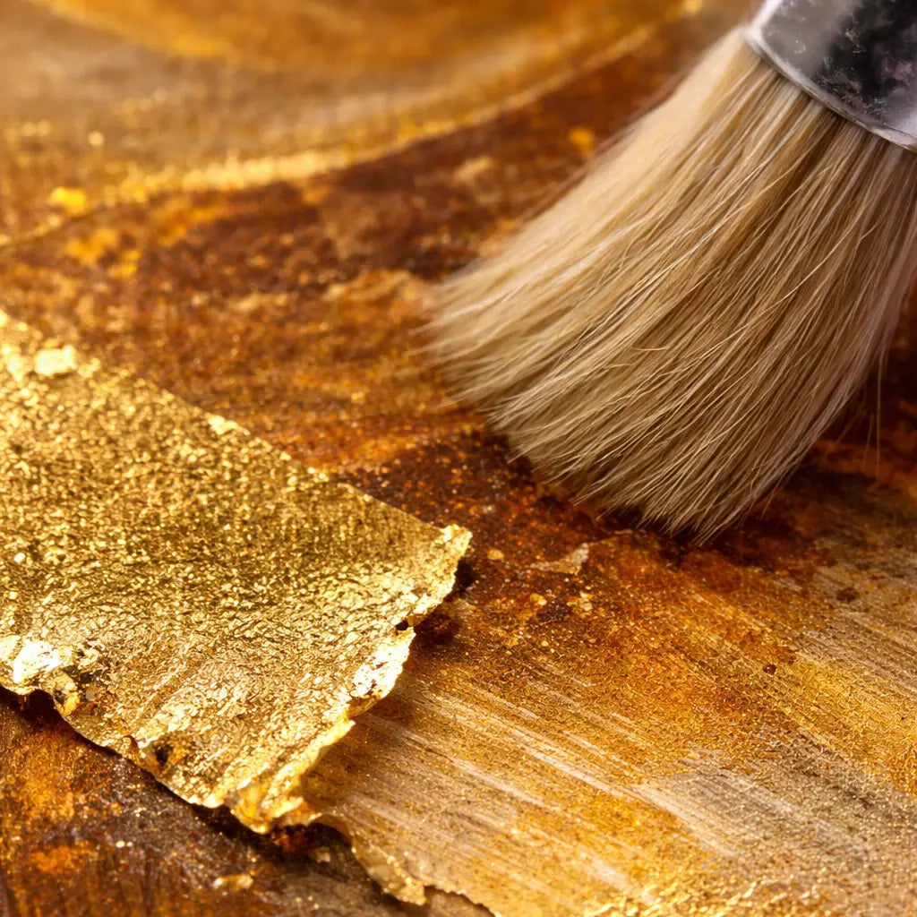 Macro close-up of hand-applied gold leaf on original acrylic painting, showing textured brushstrokes, irregular torn leaf edges, burnish marks and reflective surface sheen under studio lighting.