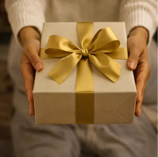 Hands holding a white gift box wrapped with a satin gold ribbon, symbolising a thoughtful and meaningful art gift.
