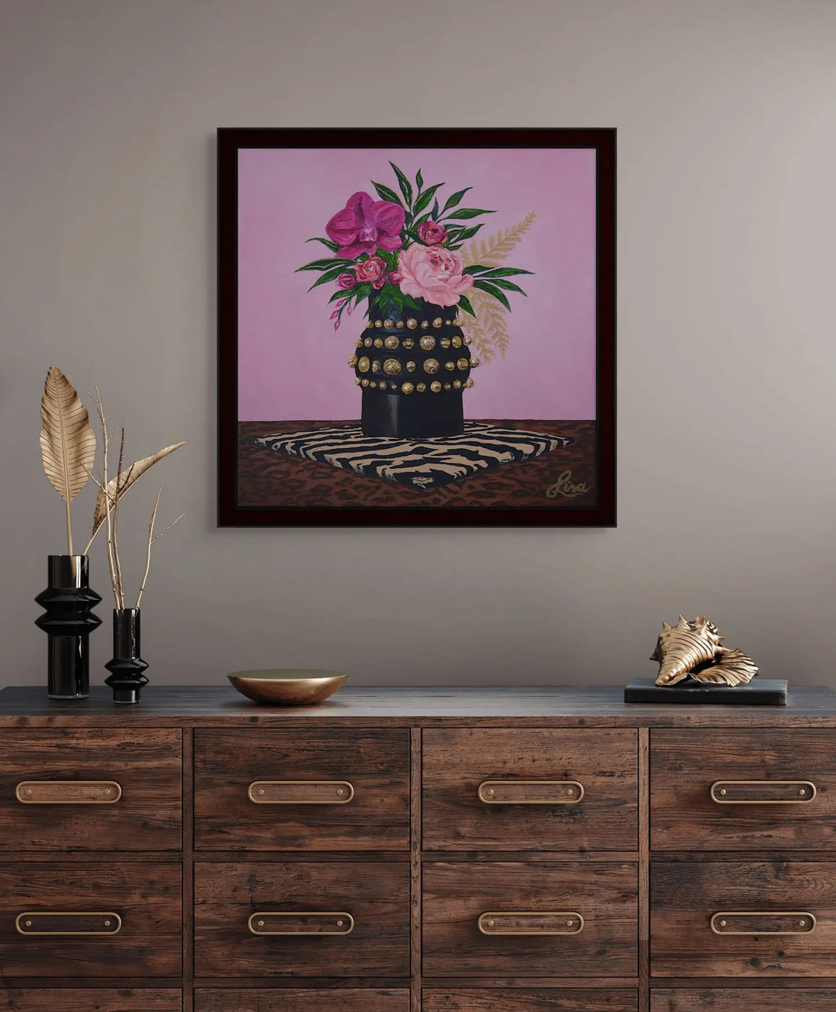 Original artwork styled in a black frame above timber drawers in a warm interior.